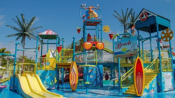 Parque acuático con toboganes, una máquina de olas y una torre de salvavidas.