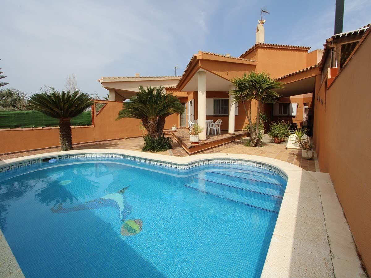 A swimming pool with a tiled edge, surrounded by a patio area with chairs and potted plants.