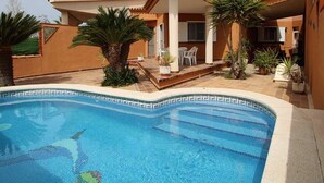 Piscina com borda em azulejo, rodeada por um espaço de terraço com cadeiras e plantas em vasos.