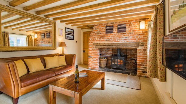 A cozy living room with a brick fireplace, a leather sofa, and wooden beams on the ceiling. - The Oast by Bloom Stays - charming oast house in beautiful countryside (Newenden)