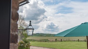 A view from a balcony overlooking a grassy field with a wooden fence, a green umbrella, and a lantern. - The Oast by Bloom Stays - charming oast house in beautiful countryside (Newenden)
