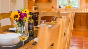 A dining table set with white plates, wine glasses, and a bottle of wine. There is a vase with flowers on the table. - The Oast by Bloom Stays - charming oast house in beautiful countryside (Newenden)
