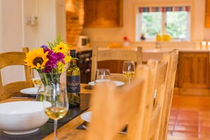 A dining table set with white plates, wine glasses, and a bottle of wine. There is a vase with flowers on the table. - The Oast by Bloom Stays - charming oast house in beautiful countryside (Newenden)