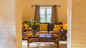 A cozy living room with a brown leather sofa, yellow cushions, and a wooden coffee table with a vase of flowers. - The Oast by Bloom Stays - charming oast house in beautiful countryside (Newenden)