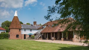 A traditional brick building with a conical roof, a white house with a grey roof, and a covered outdoor area with wooden benches. - The Oast by Bloom Stays - charming oast house in beautiful countryside (Newenden)