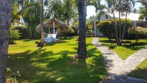 A tropical garden with a hammock, a stone pathway, and a building with a decorative facade.