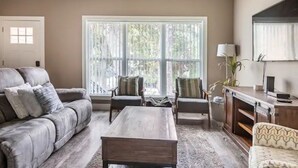 A living room with a grey sofa, two armchairs, a coffee table, and a TV stand.