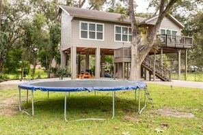 Una casa de dos pisos con un porche cubierto y un trampolín en el jardín.