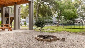 A covered outdoor area with a picnic table and a fire pit surrounded by gravel.
