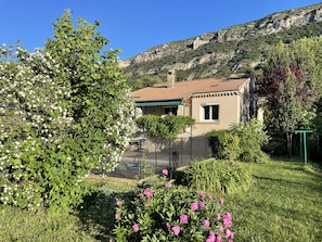 Una casa amb teulada d'àmples rajoles, envoltada de verdura exuberant i plantes amb flors.