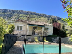 Una casa amb piscina, envoltada d'una terrassa de fusta i una zona tancada per una tanca.