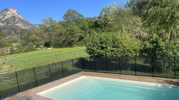 Ein rechteckiger Swimmingpool mit Holzboden, umgeben von einem schwarzen Maschendrahtzaun, mit einem Berg im Hintergrund.