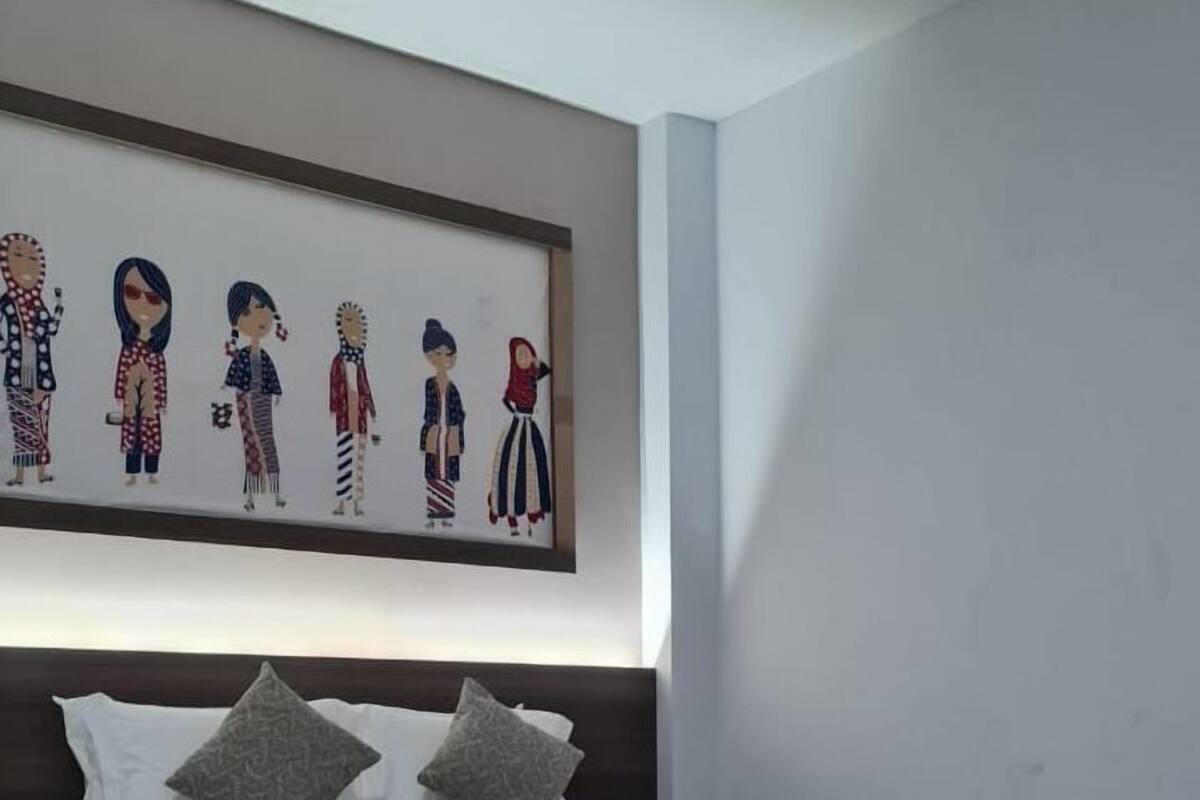 Een netjes opgemaakt bed met een bedspreide en kussens met een patroon, een groot gekaderd kunstwerk erboven en een vloerkleed met een patroon.