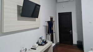 A hallway with a mounted TV, a coat rack, a door, and a trash bin. - KingKabba Guest House Wonosobo (Wonosobo)