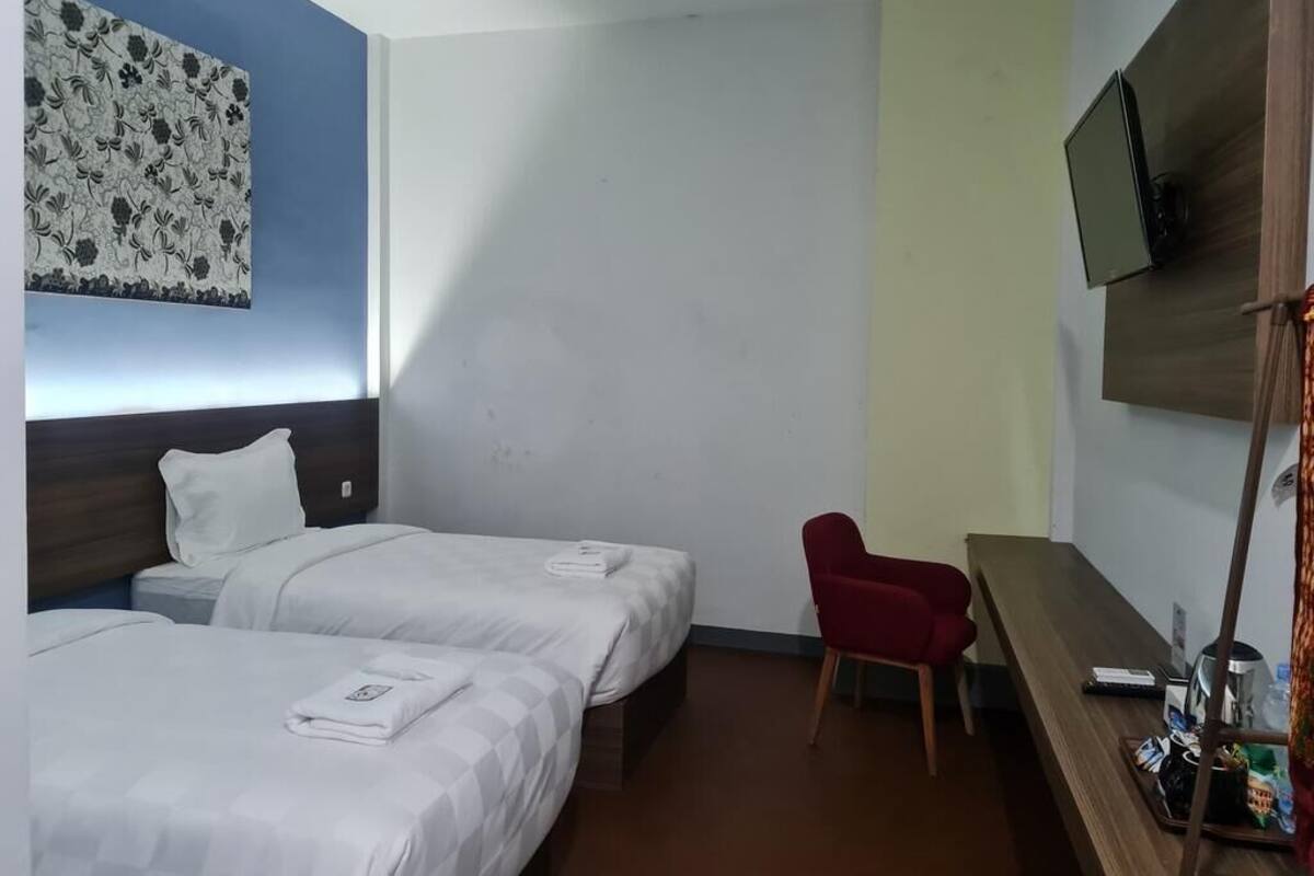 Hotelkamer met twee bedden, een rode stoel, een televisie en een houten bureau met een dienblad.
