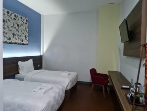 Habitación de hotel con dos camas, una silla roja, un televisor y un escritorio de madera con una bandeja de objetos.