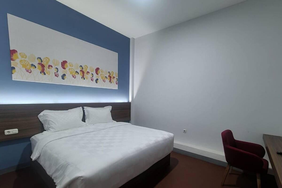 Een hotelkamer met een groot bed, een rode stoel, een houten bureau en een muur met een kleurrijk abstract schilderij.