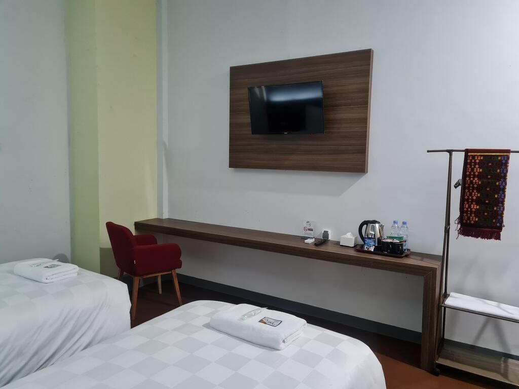 Ett hotellrum med två sängar, ett skrivbord, en TV som är monterad på väggen och en liten sittgrupp.