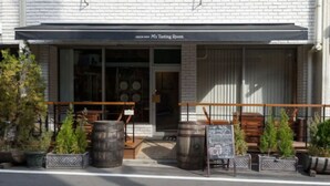 Tiilestä rakennettu rakennus, jonka sisäänkäynnin yläpuolella on kyltti, jossa lukee ”M’s Tasting Room”. Ulkona on puisia tynnyreitä ja ruukuissa olevia kasveja.