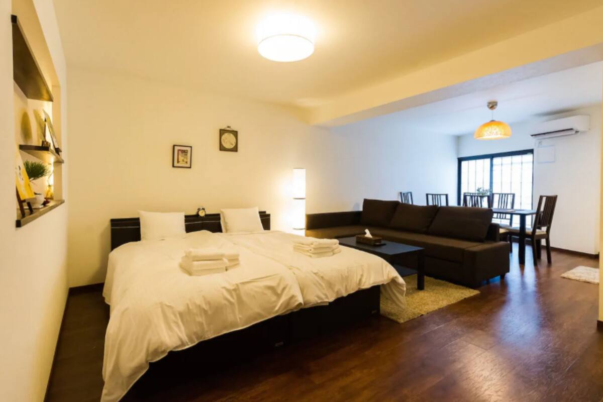 Quarto de hotel com uma cama grande, um sofá, uma mesa de centro e uma área de refeições com cadeiras e uma mesa.