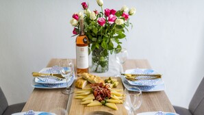 Una mesa dispuesta para una comida, con una botella de vino, un florero y una selección de quesos y embutidos.