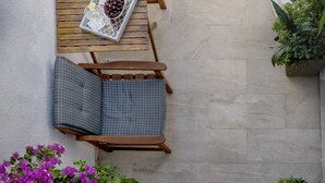 Un patio con dos sillas de madera y una mesa, un pequeño jardín con plantas y una pared blanca.
