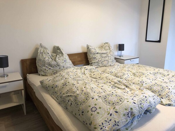 A neatly made bed with patterned bedding, a bedside table with a lamp, and a wall-mounted mirror. - Pension Jägerschenke (Luhe-Wildenau)