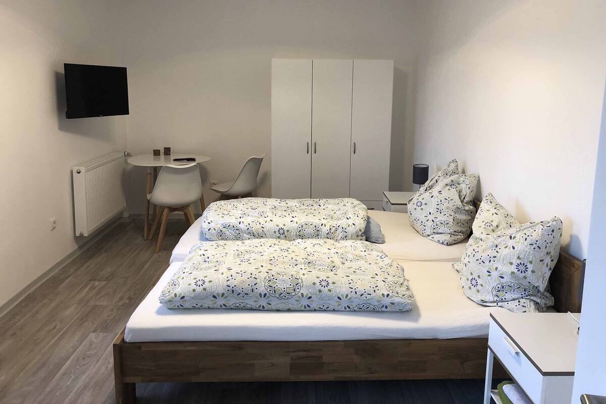 A bedroom with a bed, two chairs, a desk, a wardrobe, and a TV.