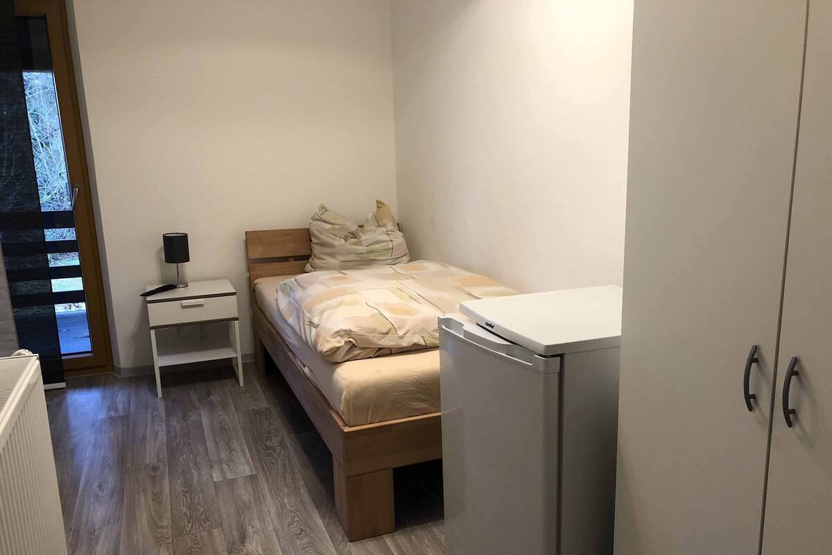 A small, compact bedroom with a bed, a nightstand, a desk, and a wardrobe.