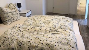 A bedroom with a bed, a nightstand, a lamp, a mirror, and a door. - Pension Jägerschenke (Luhe-Wildenau)