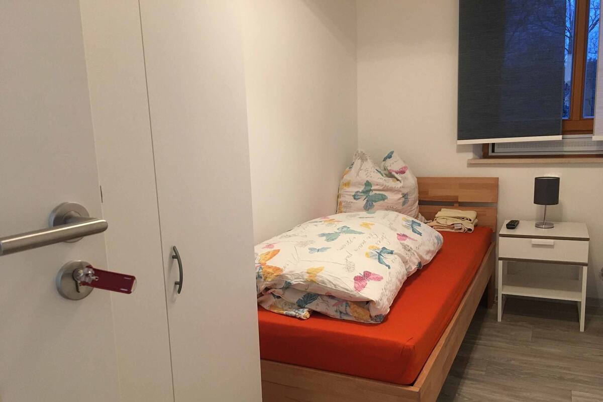 A bedroom with a bed, a nightstand, a lamp, and a window.