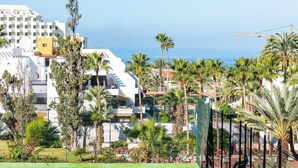 A coastal hotel with multiple white buildings, palm trees, and a tennis court.