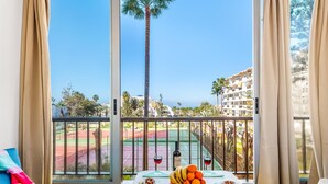 A balcony with a view of a tennis court, palm trees, and a building.