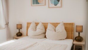 A bed with two pillows, a bedside lamp, and a small table with another lamp. - Alex 12 "Meeresleuchten" 1.O.G.  (Rostock)