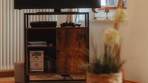 A living room with a television on a stand, a wooden coffee table, a remote control, a lamp, and a plant. - Alex 12 "Meeresleuchten" 1.O.G.  (Rostock)