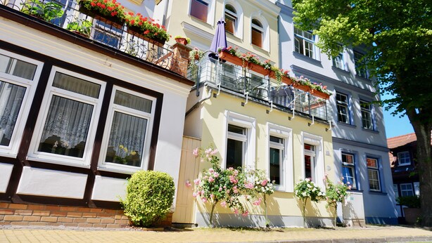 A multi-story building with balconies adorned with flowers, windows with white frames, and a brick facade. - Alex 12 "Meeresleuchten" 1.O.G.  (Rostock)