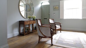A room with wooden flooring, a large mirror, two upholstered chairs, a side table with a vase, and a door in the background. - Elegant Chelsea Townhouse On Quaint Street (London)