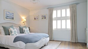 A bedroom with a large bed, two wall-mounted lamps, and a window with curtains. - Elegant Chelsea Townhouse On Quaint Street (London)