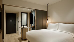 Una habitación de hotel moderna con una cama grande, una mesita de noche, un espejo y un pequeño escritorio.