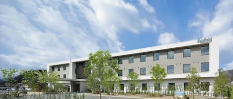 A modern hotel building with a flat roof, multiple windows, and a parking lot in front.