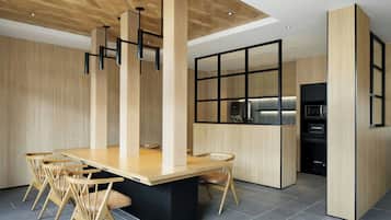 A modern kitchen with a central island, wooden chairs, and a black countertop.