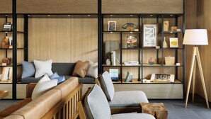 A modern living room with a sofa, chairs, a wooden bookshelf, and a floor lamp.
