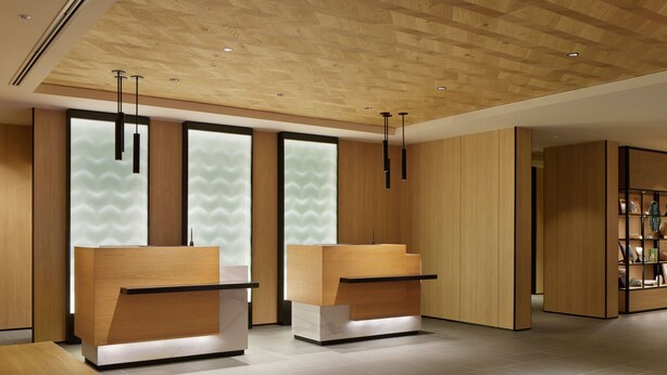 Una zona de recepción moderna con mostradores de madera, suelo de baldosas y techo con paneles de madera.