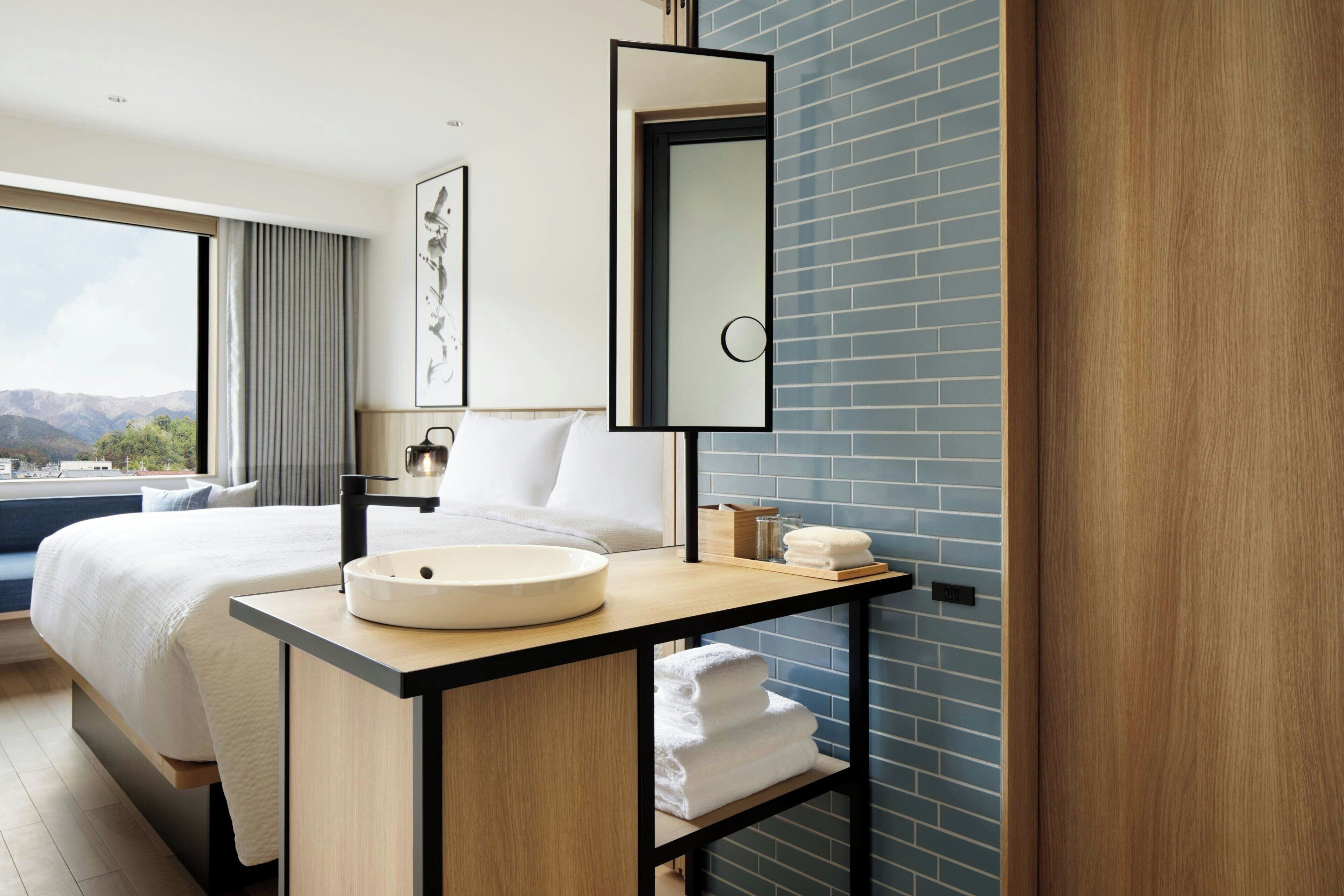 Une chambre d’hôtel moderne avec un grand lit, un lavabo rond, un miroir et une vue sur les montagnes.