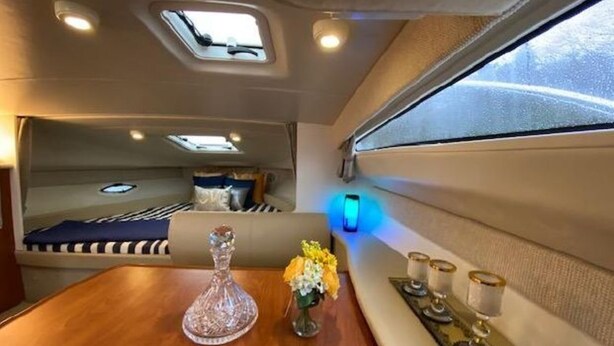 A compact interior with a bed, a small table with a vase of flowers, and a window with a view.