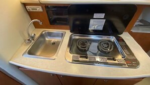 A compact kitchen with a sink, two burners, and a small window.