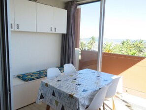 A balcony with a table and chairs, a sofa, and a view of palm trees and the sea.