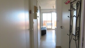 A hallway leading to a bedroom with a bed, a window, and a door with a metal gate.