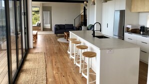 A modern kitchen with a central island, bar stools, and a dining area with a sofa and table. - A view like none other (Cooks Beach)