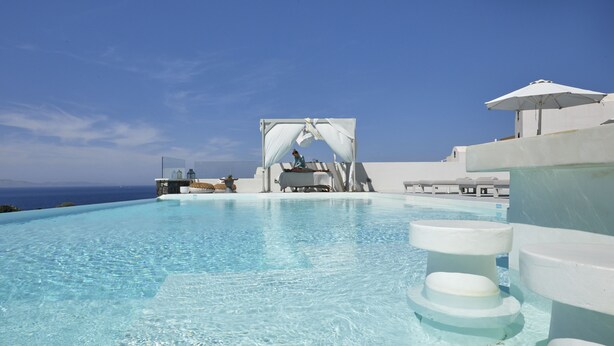An infinity pool with clear water, a white canopy structure, and a view of the ocean.